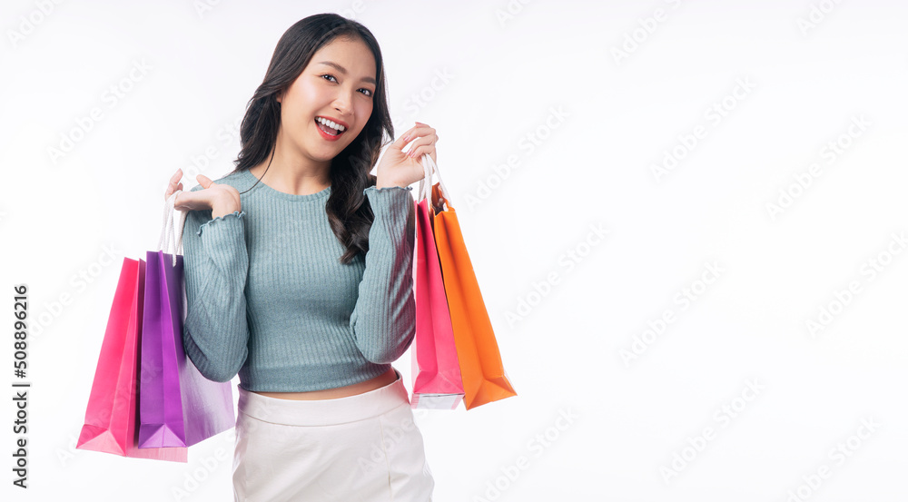 Enjoyment excited asian woman carry shopping bags standing on white background. Trendy happy shopper consumer carefree young girl holding shopping paper bags with copy space over isolated background.