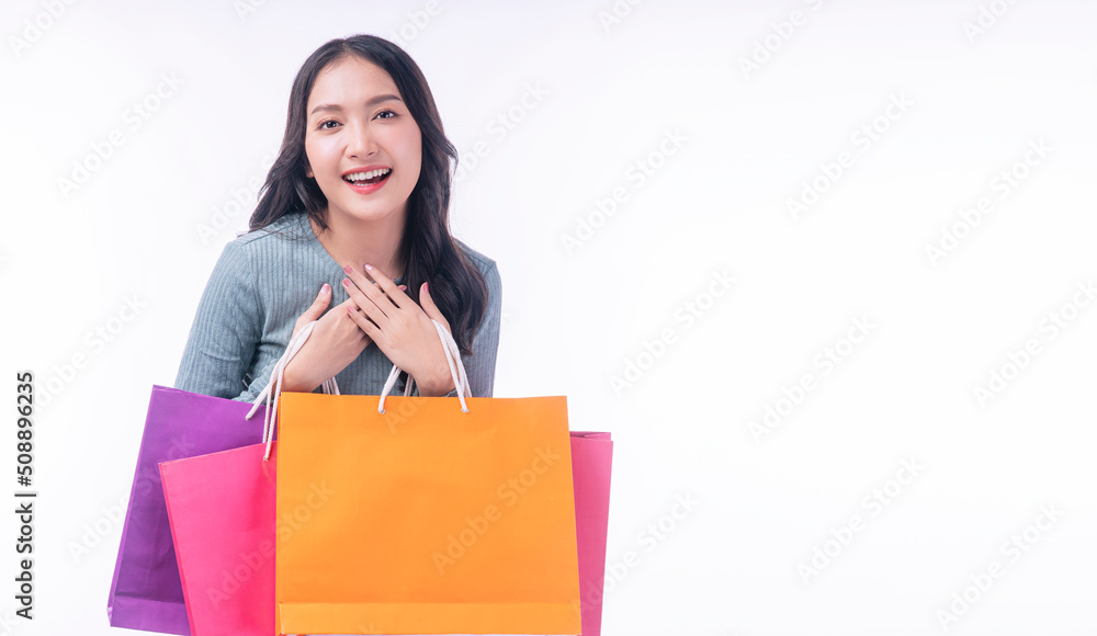 Enjoyment excited asian woman carry shopping bags standing on white background. Trendy happy shopper consumer carefree young girl holding shopping paper bags with copy space over isolated background. Enjoyment excited asian woman carry shopping bags standing on white background. Trendy happy shopper consumer carefree young girl holding shopping paper bags with copy space over isolated background.