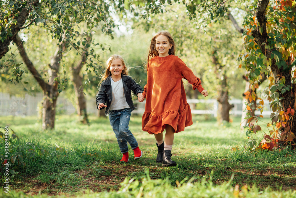 Fototapeta premium Children running , dancing plays on the meadow. Girls having fun. Cute little longhair blonde girl dancing at sunset park. Selective focus