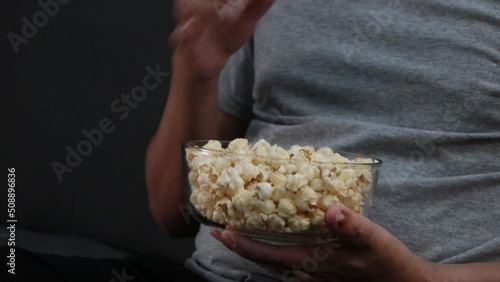 Man eating popcorn in a glass cup on the sofa. while watching movies at home.
