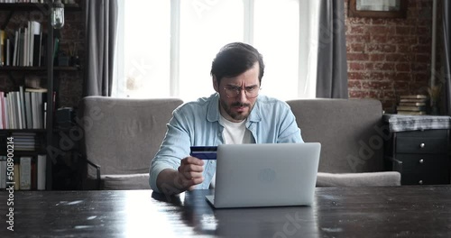 Angry millennial male in glasses hold prepaid card look on pc screen feel mad annoyed get payment rejection after entering wrong password. Worried young man overspend money on electronic bank account photo