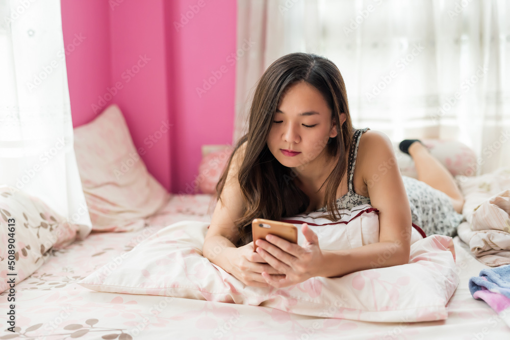asian woman using mobile phone on a pink mattress bed in morning asian woman using mobile phone on a pink mattress bed in morning