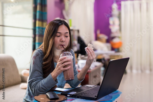 Woman drink ice chocolate, eat sandwich, and work at computer