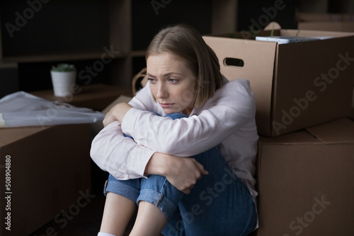 Sad young woman sits near heap of cardboard boxes with personal belongings looks upset goes through divorce, unsuccessful marriage and property division, move-out day. Eviction, mortgage debt concept