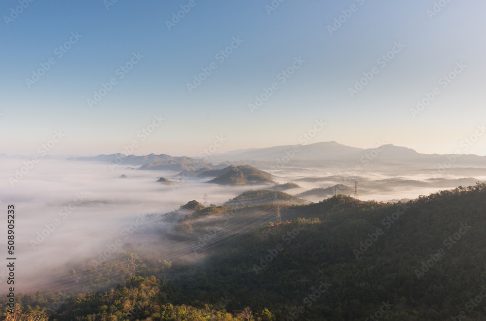 Aerial view Transmission tower in green forest and beautiful morning smooth fog. Energy and environment concept. High voltage power poles. Pang Puay, Mae Moh, Lampang, Thailand. Aerial view Transmission tower in green forest and beautiful morning smooth fog. Energy and environment concept. High voltage power poles. Pang Puay, Mae Moh, Lampang, Thailand.