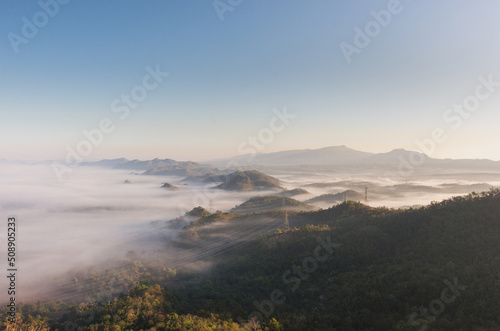 Aerial view Transmission tower in green forest and beautiful morning smooth fog. Energy and environment concept. High voltage power poles. Pang Puay, Mae Moh, Lampang, Thailand.