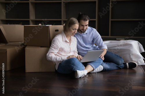 Married couple use laptop buying on-line, make order on relocation day. E-commerce services shoppers choose furniture, living room design interior ideas on internet. Moving, e-services clients concept