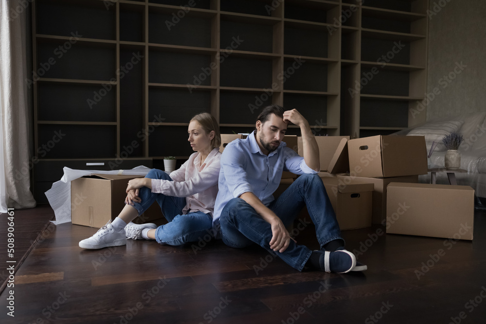 Naklejka premium Exhausted couple sit rest on floor in living room near heap of cardboard boxes look unmotivated to unpack their stuff, feel tired. Financial problems, bank debt, hard relocation day, break up concept