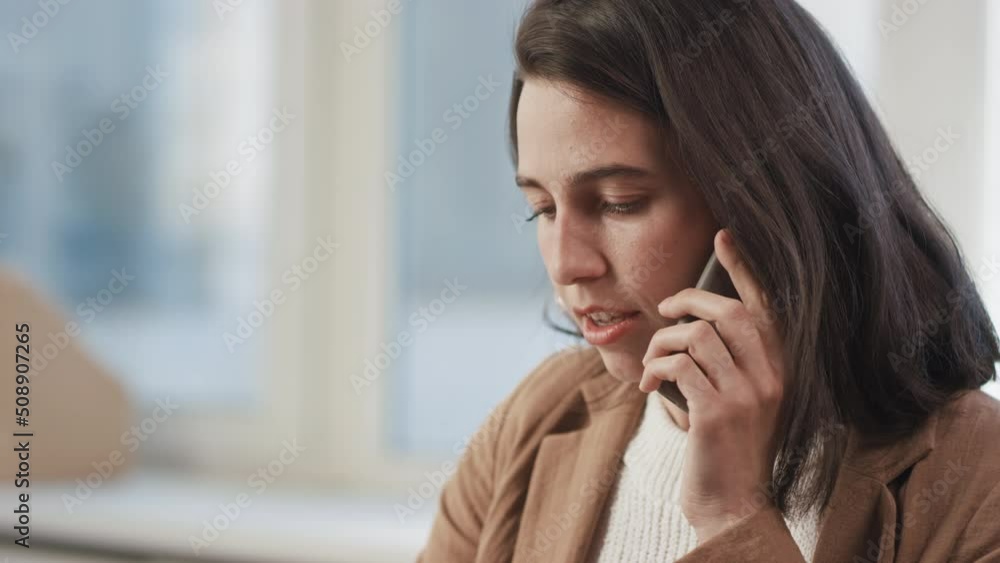 Medium close-up portrait of young woman wearing casual outfit sitting in office room talking on phone and using laptop Medium close-up portrait of young woman wearing casual outfit sitting in office room talking on phone and using laptop