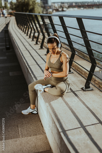 Pretty young woman with earphones takes a break after running in urban area