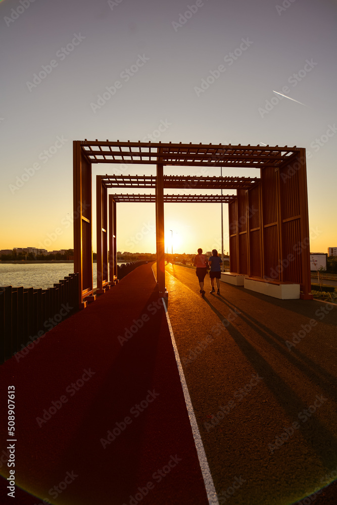 Jogging in the morning. People are running on a park next to a lake during an amazing summer sunrise. Run is a healthy way of living. People and sports.