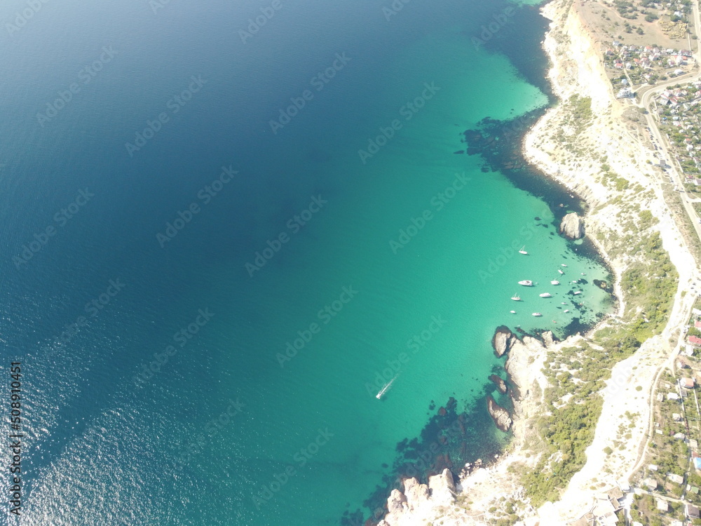 Aerial view from above on calm azure sea and volcanic rocky shores. Small waves on water surface in motion blur. Nature summer ocean sea beach background. Nobody. Holiday, vacation and travel concept