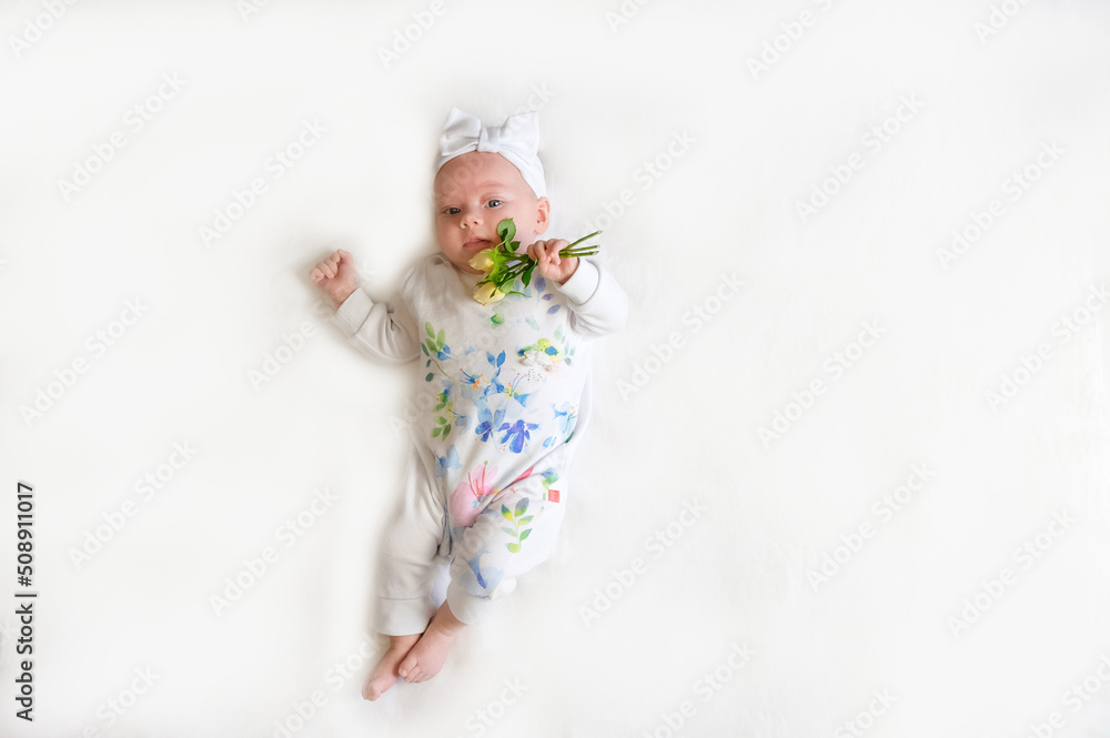 Fototapeta premium Beautiful baby girl holding a flower on white blanket. The baby girl with a bandage on his head holding a rose in his hand. The baby smiles.