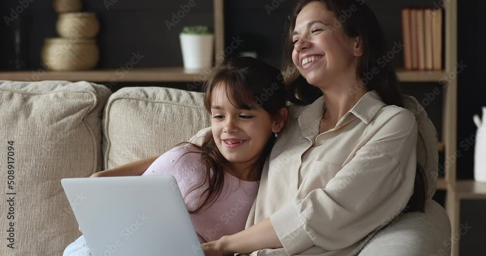 Young mom her little daughter rest on sofa with laptop, watch cartoons and movie through digital streaming on-line services, enjoy weekend at home use modern tech. Do e-shopping, make order feel happy Young mom her little daughter rest on sofa with laptop, watch cartoons and movie through digital streaming on-line services, enjoy weekend at home use modern tech. Do e-shopping, make order feel happy
