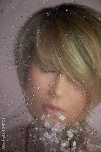 A girl with flowers behind wet glass. Nega and enjoyment of life. Eyes closed. Beauty and personal care industry. photo
