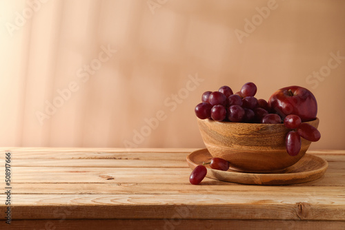 Grapes and red apple in wooden bowl over beige background. Summer kitchen table mock up for design and product display photo