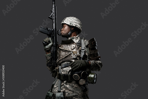 Photo of isolated on grey black soldier dressed in protective uniform posing with rifle.