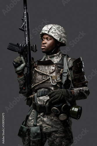 Fototapeta Portrait of african military man dressed in modern camouflage uniform holding rifle