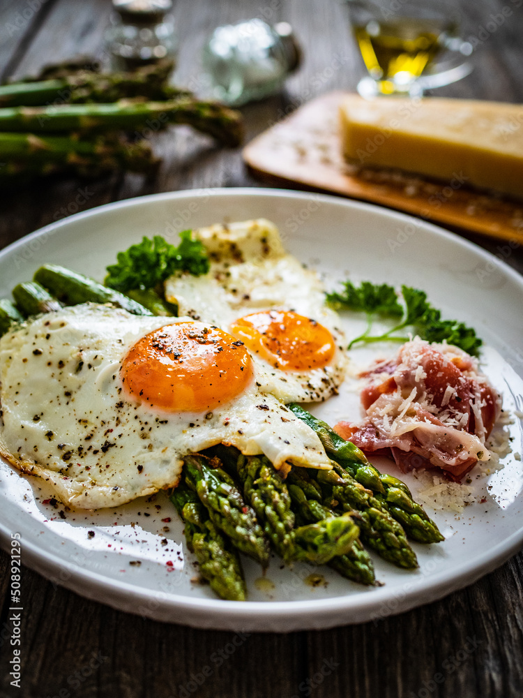 Sunny side up eggs with green asparagus fried bacon on black plate on wooden table
Sunny side up eggs with green asparagus fried bacon on black plate on wooden table