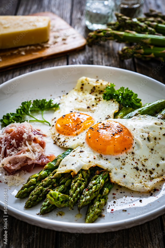 Sunny side up eggs with green asparagus  fried bacon on black plate on wooden table
