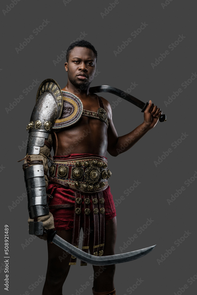 Shot of ancient gladiator of african ethnic holding twin swords isolated on gray background. Shot of ancient gladiator of african ethnic holding twin swords isolated on gray background.