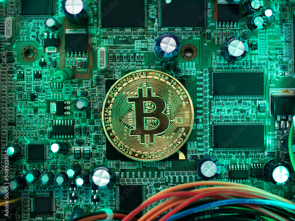 A large yellow bitcoin lies on the microprocessor of a computer board with electrical components and wires. Bitcoin as an electronic payment system. A large yellow bitcoin lies on the microprocessor of a computer board with electrical components and wires. Bitcoin as an electronic payment system.