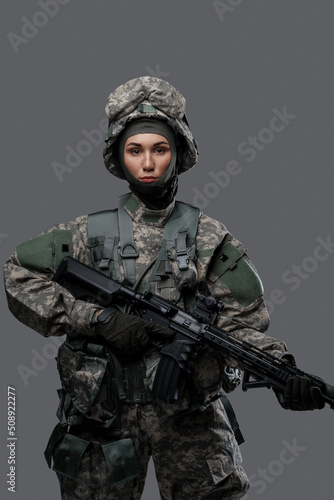 Shot of special forces woman dressed in protective uniform holding rifle isolated on gray background.