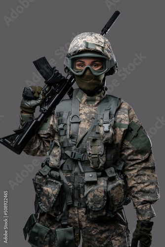 Shot of militant woman dressed in uniform with helmet and eyewear holding rifle.