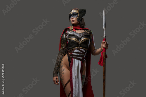 Vászonkép Studio shot of wild female warrior from past with painted face holding spear isolated on grey background