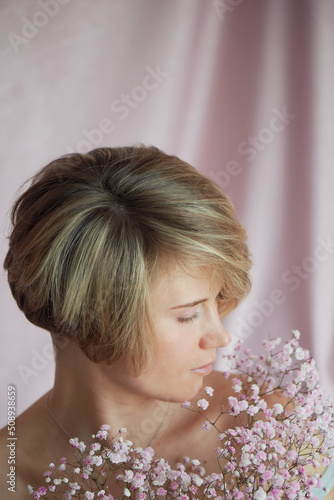 Portrait of a girl on a pink background with flowers. Tenderness and feminine. The sphere of beauty and women's health. Short haircut, blonde hair