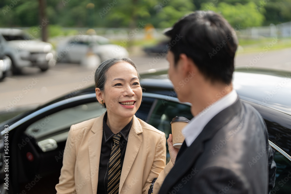 Happy senior old asian businesswoman discussion talking about new project with young asian male colleague at car park. Happy senior old asian businesswoman discussion talking about new project with young asian male colleague at car park.
