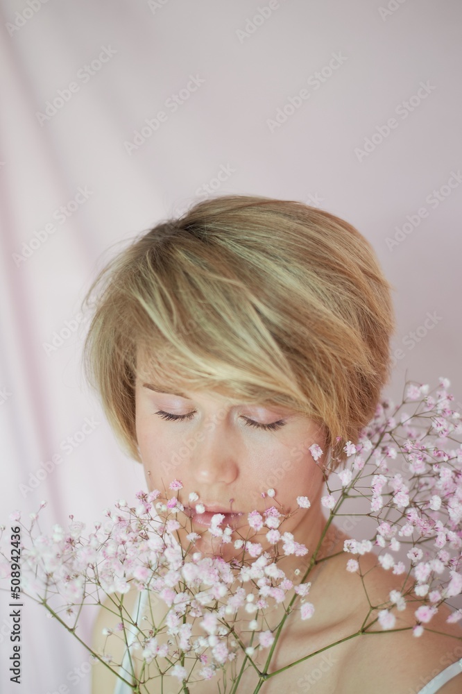 Portrait of a girl on a pink background with flowers. Tenderness and feminine. The sphere of beauty and women's health. Short haircut, blonde hair Portrait of a girl on a pink background with flowers. Tenderness and feminine. The sphere of beauty and women's health. Short haircut, blonde hair