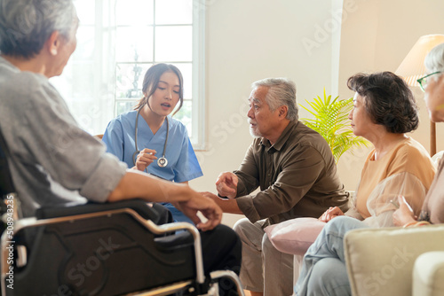 happiness Cheerful elderly woman and men talking with female caregiver nurse doctor having health checking consult at living area Caretakers with senior couple sitting in living room at nursing home