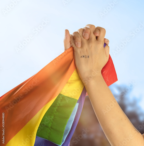 hands of two girls holding each other with the word love in the palm of the hand outdoors waving gay flag