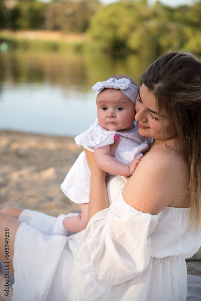Fototapeta premium mom with a newborn baby sits on the beach, on the sand. mom holds a newborn baby in her arms.