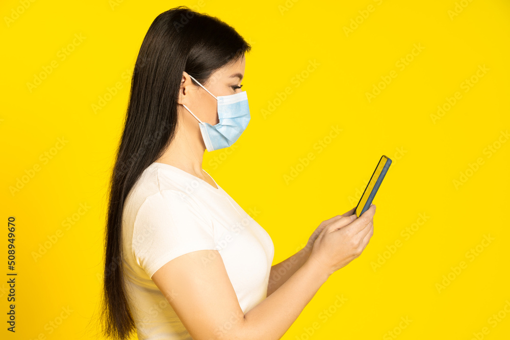 Half length profile of asian middle aged woman in medical face mask, holding smartphone in hands reading news or important information Half length profile of asian middle aged woman in medical face mask, holding smartphone in hands reading news or important information