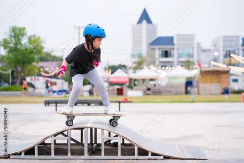 Child or kid girl playing surfskate or skateboard in skating rink or sports park at parking to wearing safety helmet elbow pads wrist and knee support photo
