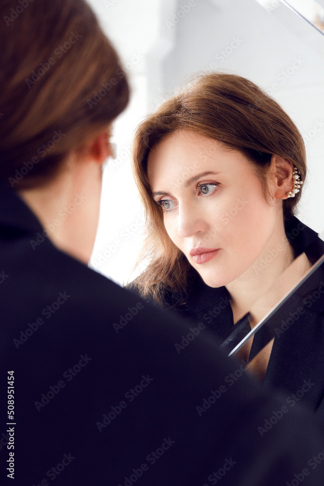 A woman stands in front of a mirror and looks away. Woman and reflection in the mirror. A woman stands in front of a mirror and looks away. Woman and reflection in the mirror.