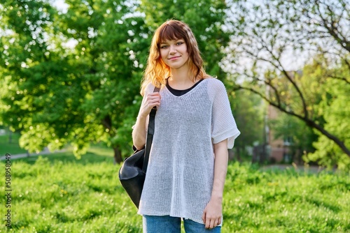 Outdoor portrait of beautiful smiling teen female student with backpack looking at camera