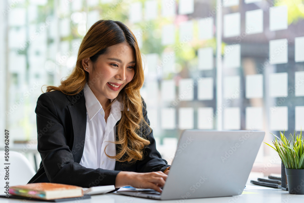 Happy young asian businesswoman sitting on her workplace in the office. Young woman working at laptop in the office. Happy young asian businesswoman sitting on her workplace in the office. Young woman working at laptop in the office.