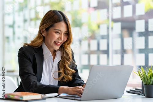 Photos Happy young asian businesswoman sitting on her workplace in the office