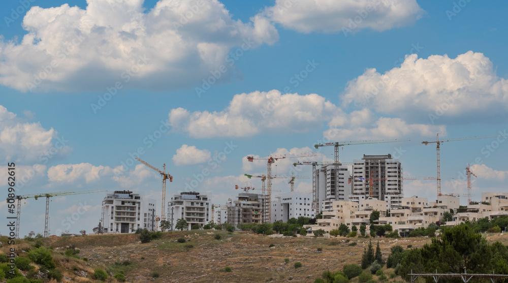 Modiin, Israel, May 21, 2022.Construction of a multi-story residential building and a large new residential area overlooking a green park with trees and a lawn next to residential buildings against a