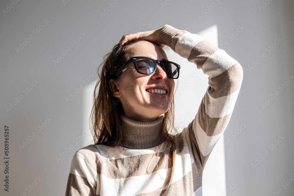 Smiling young woman in sunglasses fixing her hair against a white wall. Smiling young woman in sunglasses fixing her hair against a white wall.