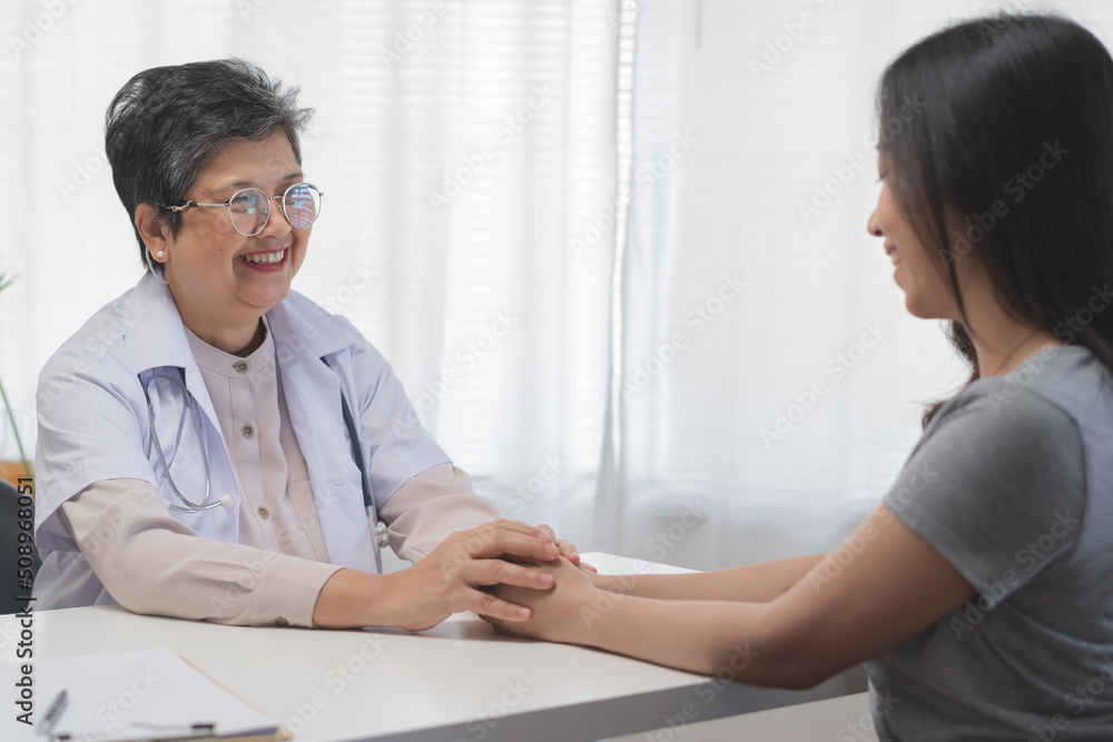 Obraz premium Aged asian physician psychiatrist, general woman doctor holds the patient's hand to encourage the patient to see the doctor at the appointment at clinic, hospital. Health care, check up medical.