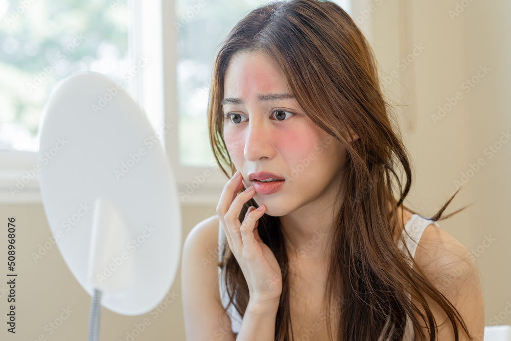 Dermatology, puberty asian young woman, girl looking into mirror, allergy presenting an allergic reaction from cosmetic, red spot or rash on face. Beauty care from skin problem by medical treatment. Dermatology, puberty asian young woman, girl looking into mirror, allergy presenting an allergic reaction from cosmetic, red spot or rash on face. Beauty care from skin problem by medical treatment.