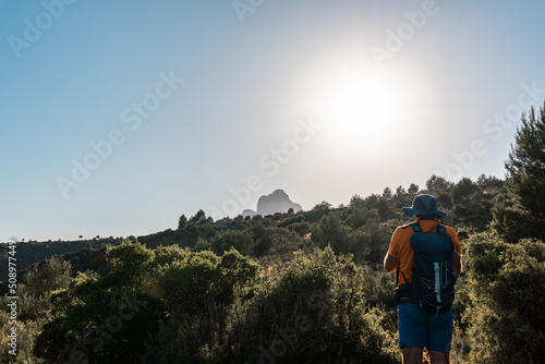 Rear view of a hiker walking through the mountains with the sun in front  on a hot summer afternoon.