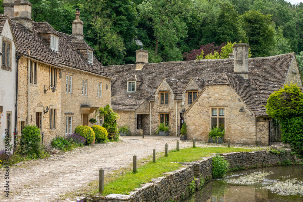 honey coloured Cotswold stone houses and Bybrook river in Castle Combe ...