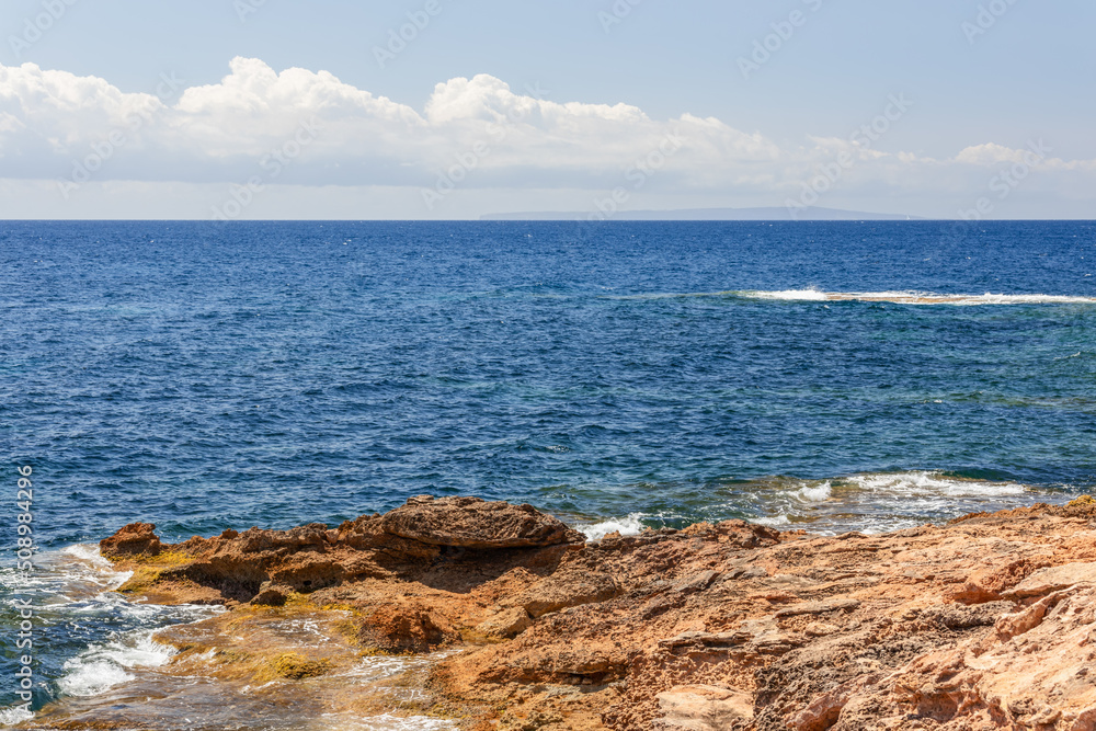 Emerald blue Mediterranean warm water gently caresses orange rocky cliff, Ibiza, Balearic Islands, Spain Emerald blue Mediterranean warm water gently caresses orange rocky cliff, Ibiza, Balearic Islands, Spain