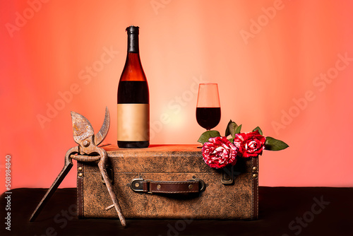 Bodegón botella de vino tinto y copa sobre una maleta vintage y fondo del atardecer muy colorido photo