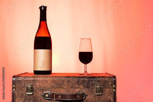 Bodegón botella de vino tinto y copa sobre una maleta vintage y fondo del atardecer muy colorido photo
